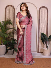 Woman wearing a pink saree with a white border indoors with plants in the background