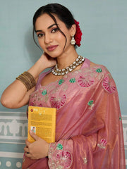 Woman in traditional pink saree with floral decorations, holding a yellow card against a light blue wall.