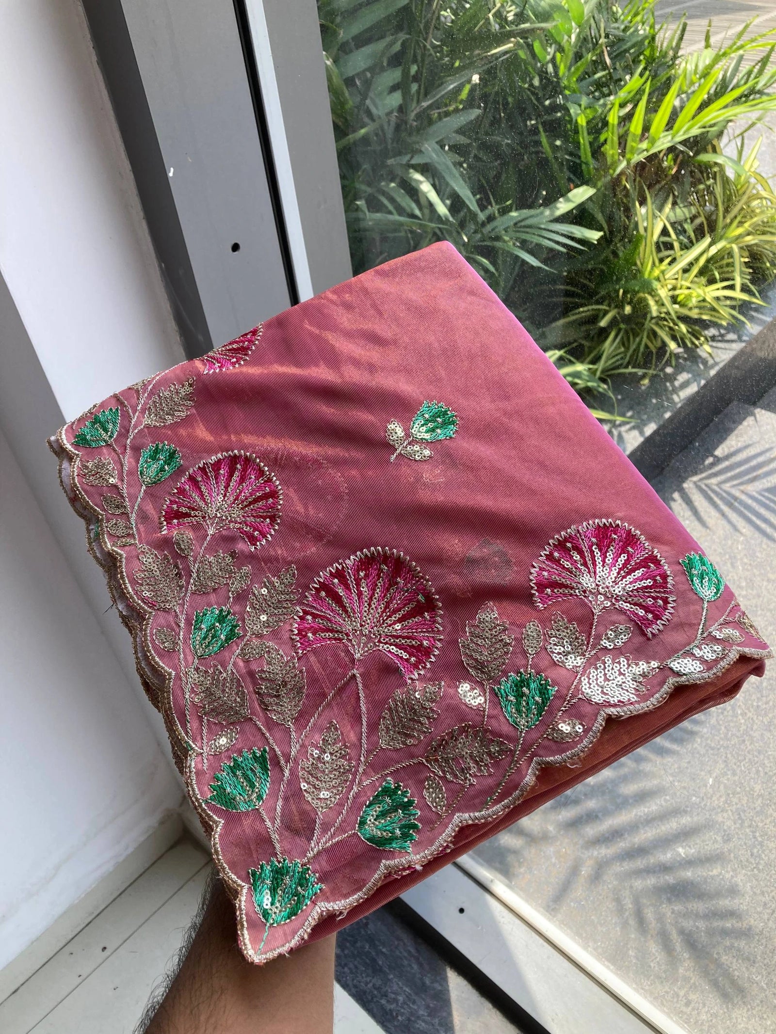 Pink embroidered fabric with green and gold details on a window sill.