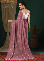 Woman in a mauve saree with white floral patterns against a dark green background