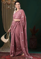 Woman wearing a mauve saree with white floral patterns, holding a beige handbag against a dark background.