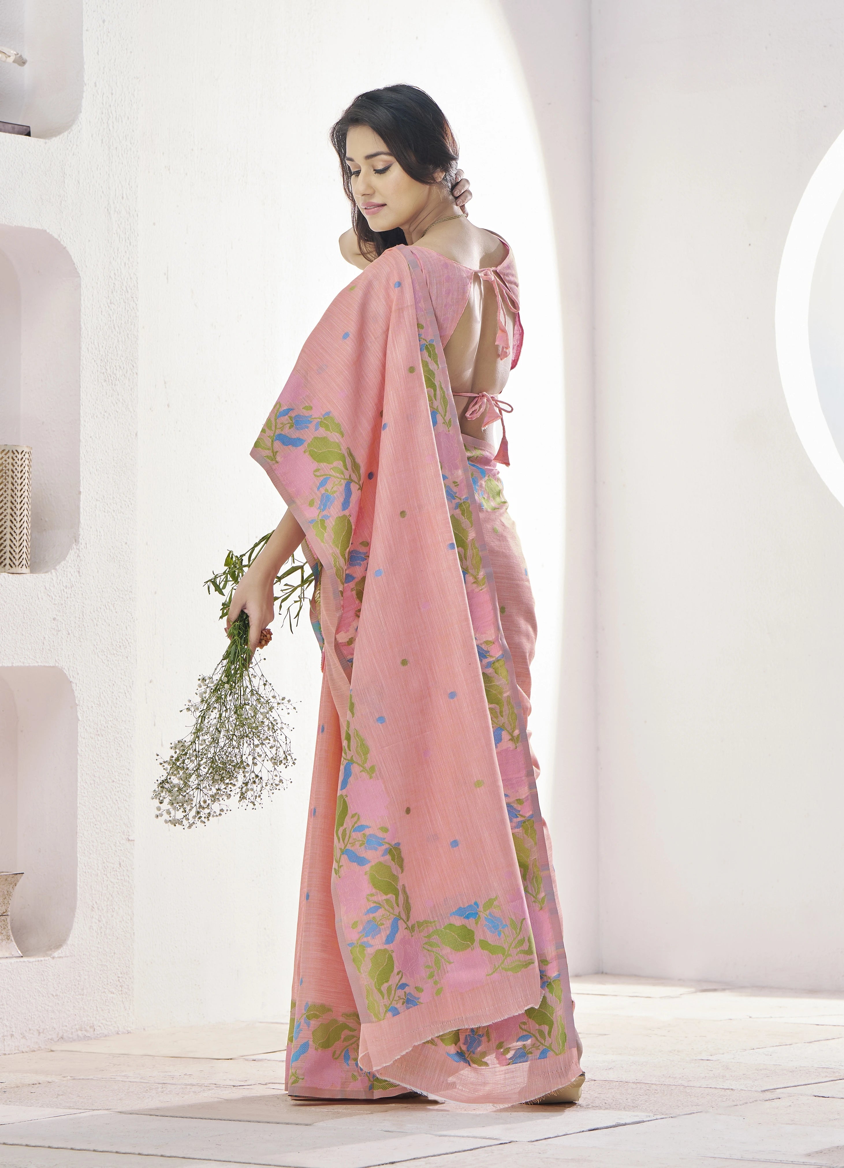 Woman wearing a pink saree with floral patterns in a minimalistic setting