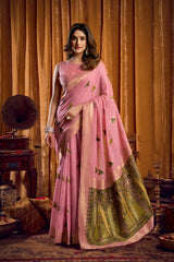 Woman in a pink saree with green border standing in an ornate room.