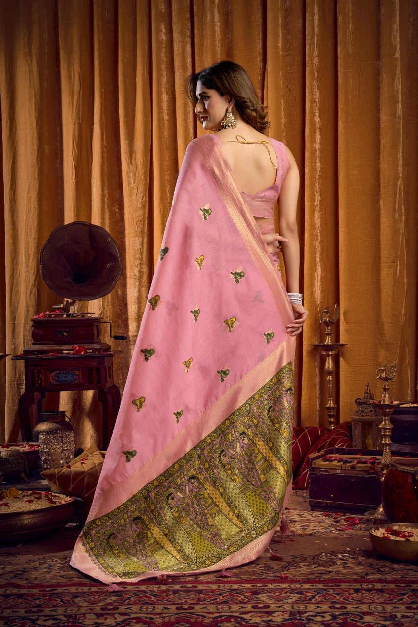Woman in a pink saree with green border standing in an ornate room.