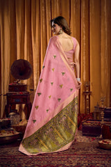 Woman in a pink saree with green border standing in an ornate room.
