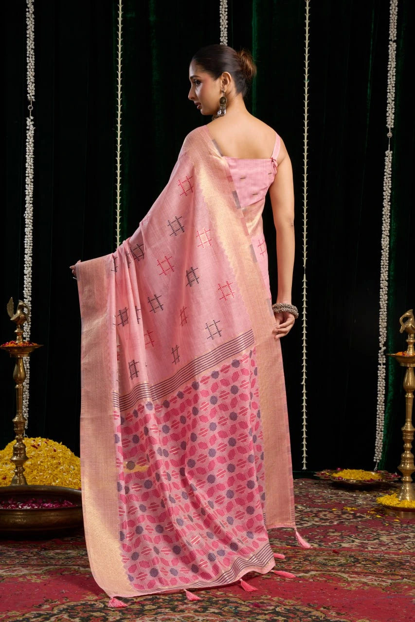 Woman in a pink saree with a black and white pattern, standing against a dark background.