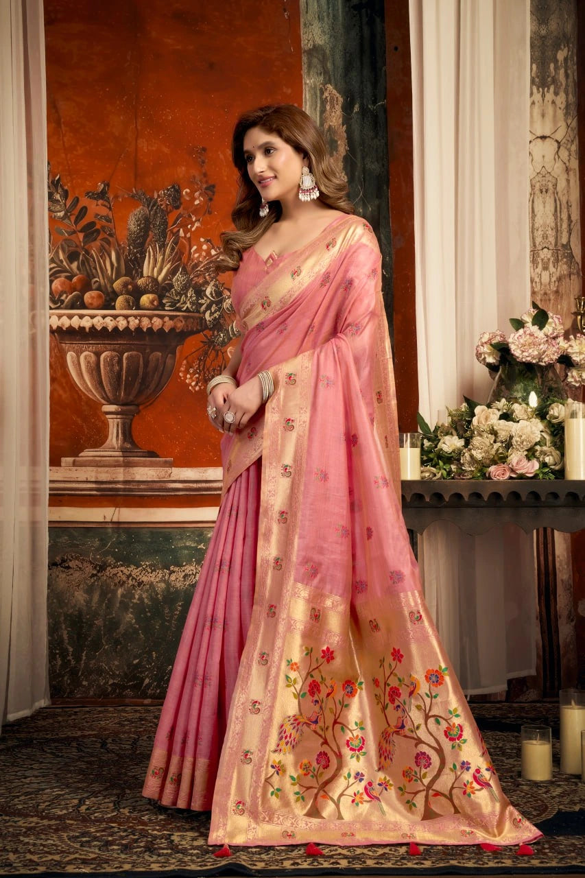 Woman in a pink saree with floral patterns standing in an elegant room.