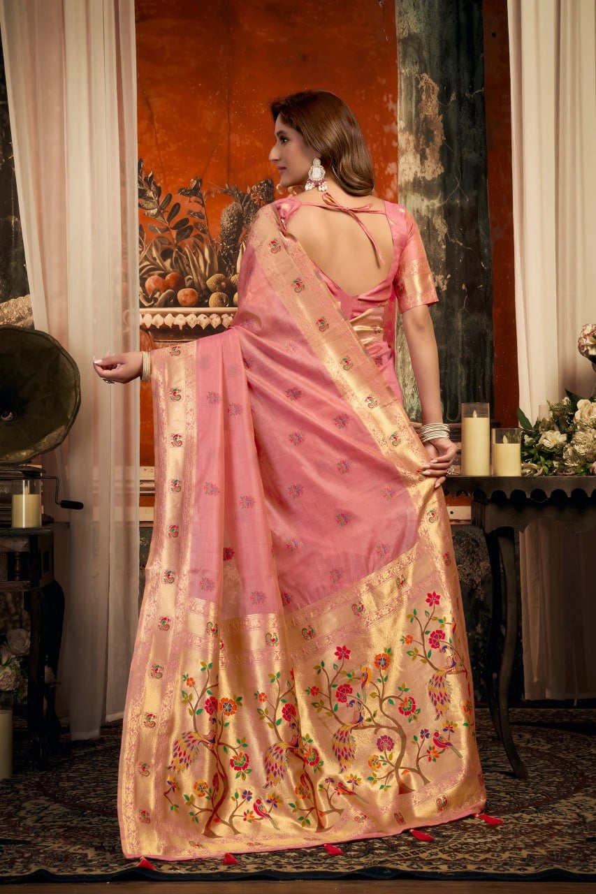 Woman in a pink saree with floral patterns standing indoors.