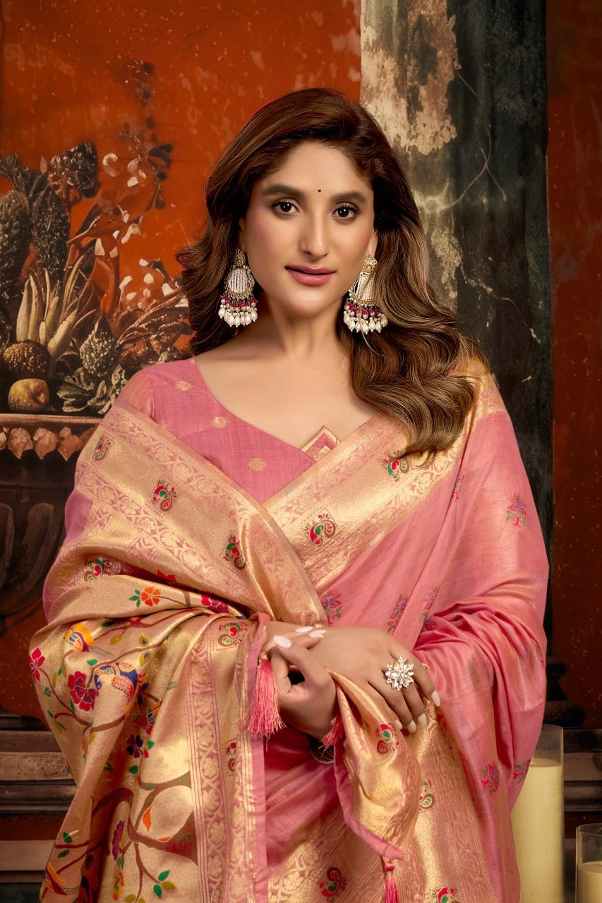 Woman wearing a traditional pink and gold saree with intricate patterns, standing against an ornate wall.