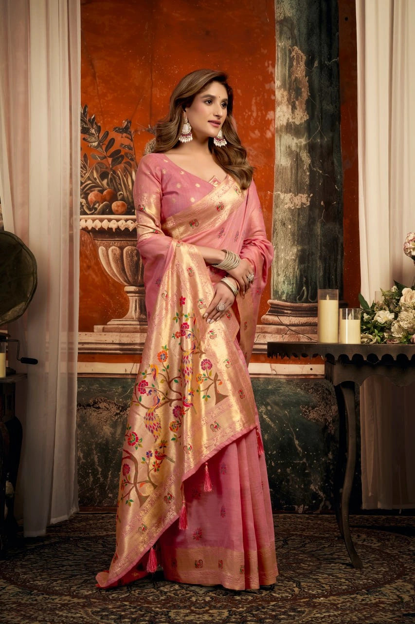 Woman in a pink saree with floral patterns in an elegant indoor setting.