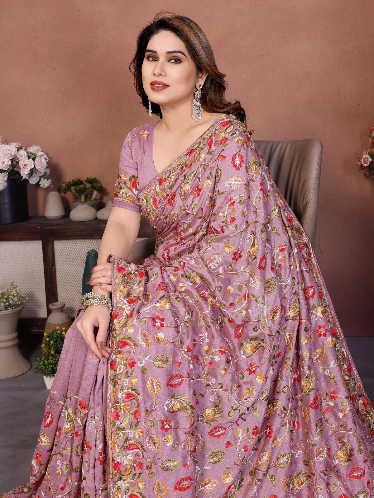 Woman wearing a floral saree sitting indoors with a neutral background
