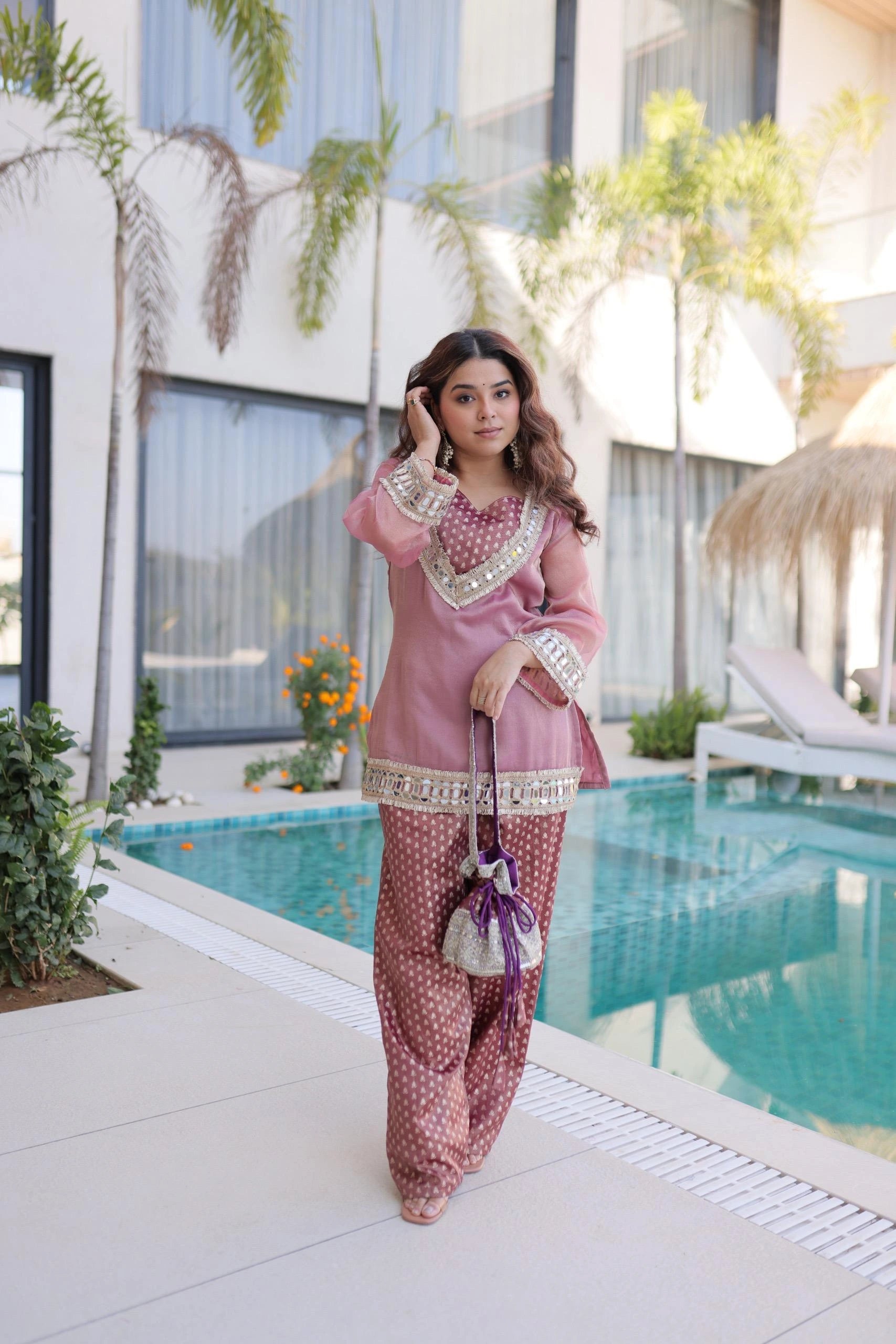 Woman in traditional outfit by a poolside with plants and modern building in the background
