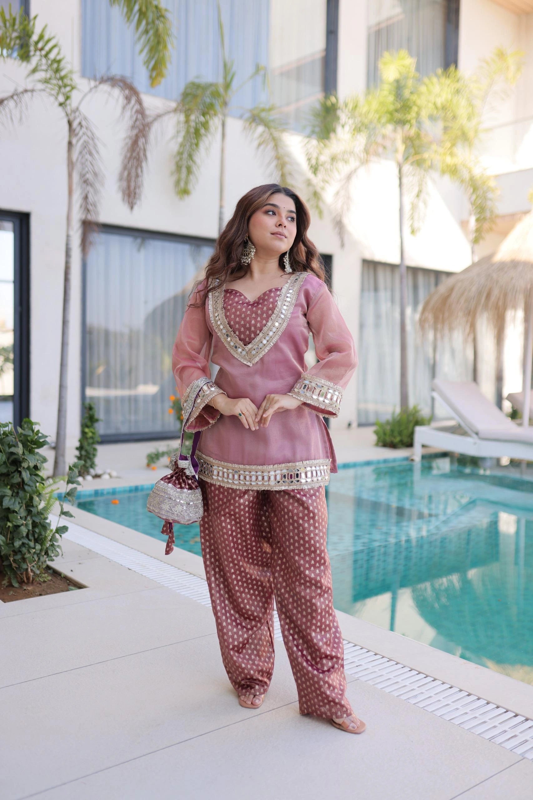 Woman in traditional outfit by a poolside with modern building and plants in the background