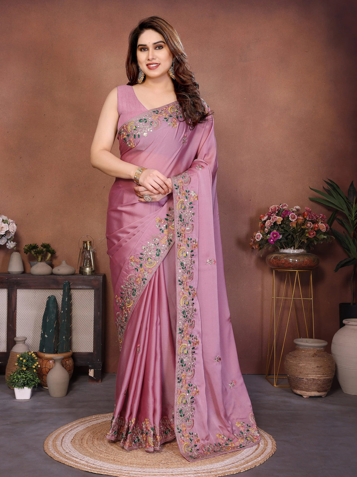 Woman wearing a pink saree with floral patterns in a decorated room.