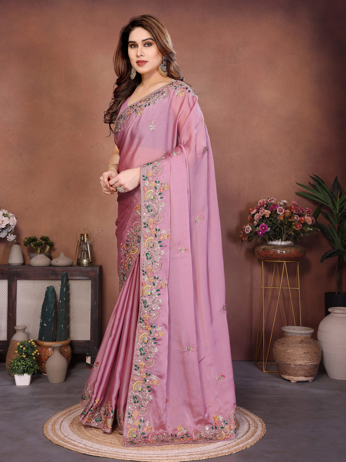 Woman wearing a pink saree with floral patterns in an indoor setting.