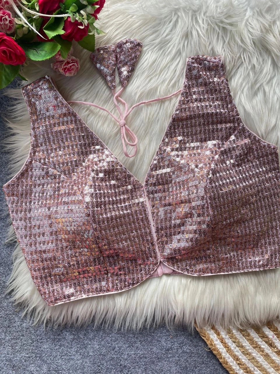 Pink sequin bralette on a textured surface with flowers in the corner