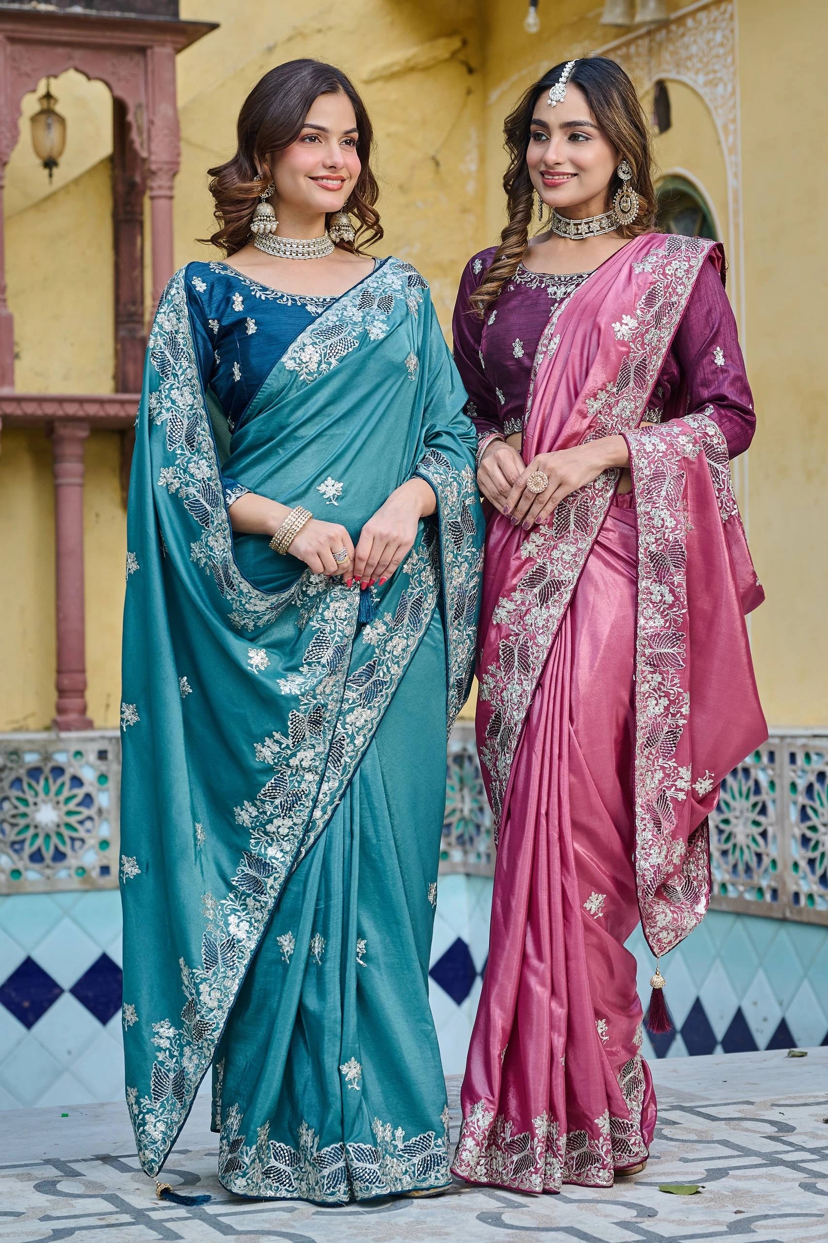 Two women in traditional sarees standing in front of a decorative wall.