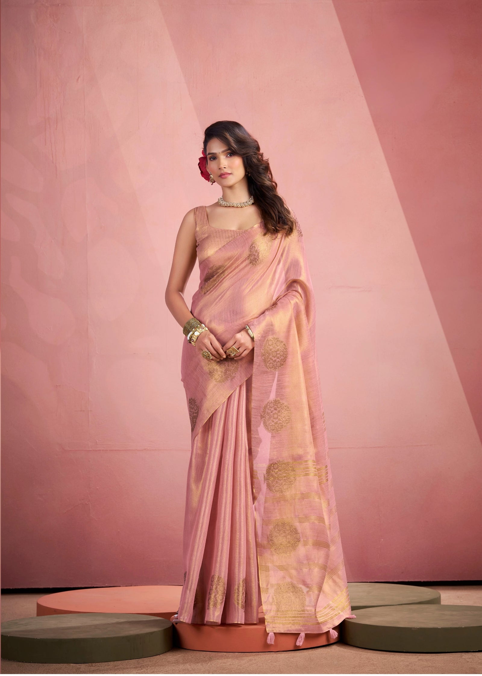 Woman wearing a pink and white saree against a stone wall.