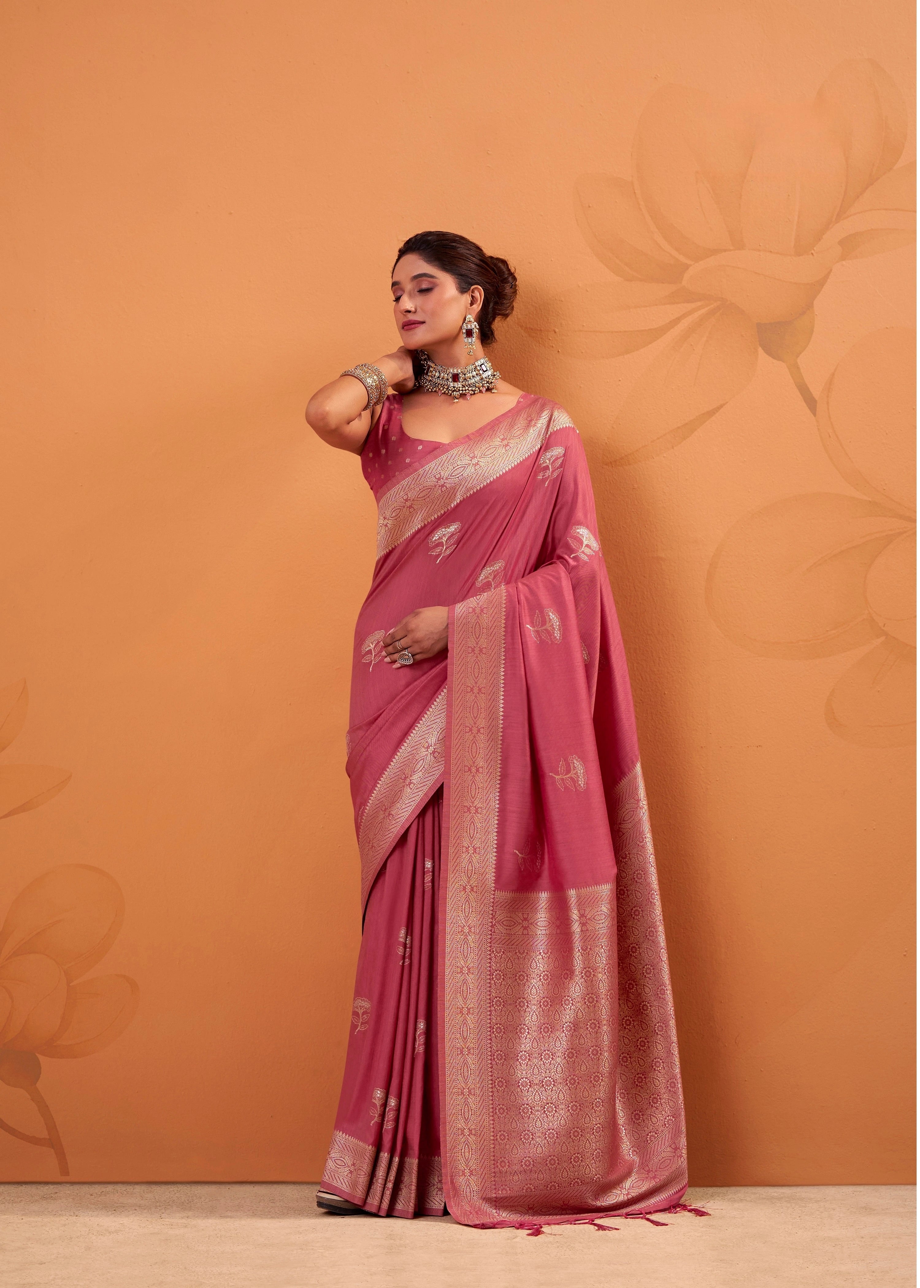 Woman wearing a pink saree with a subtle pattern against an orange background