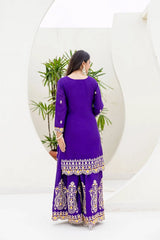 Woman wearing a purple traditional outfit with white embroidery, standing against a white background with a plant.