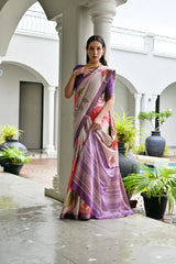 Woman in a colorful saree standing in an outdoor setting with columns and plants.