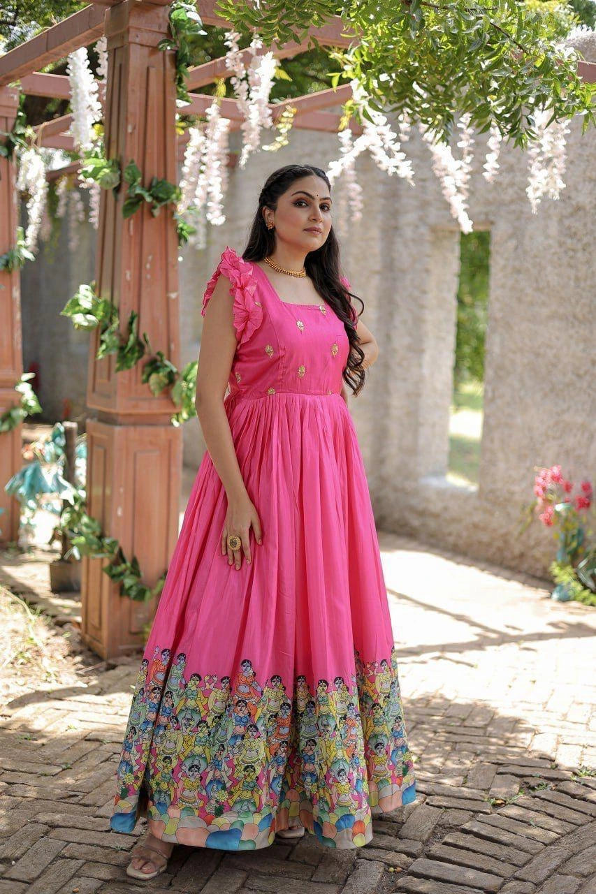 Woman in a pink dress with floral patterns standing outdoors under a decorated archway.
