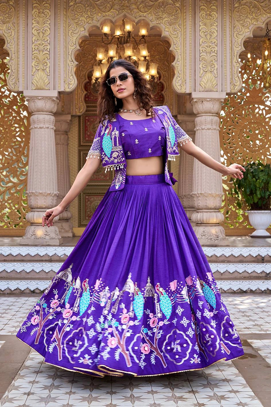 Woman in a purple embroidered traditional outfit standing in front of an ornate architectural background.