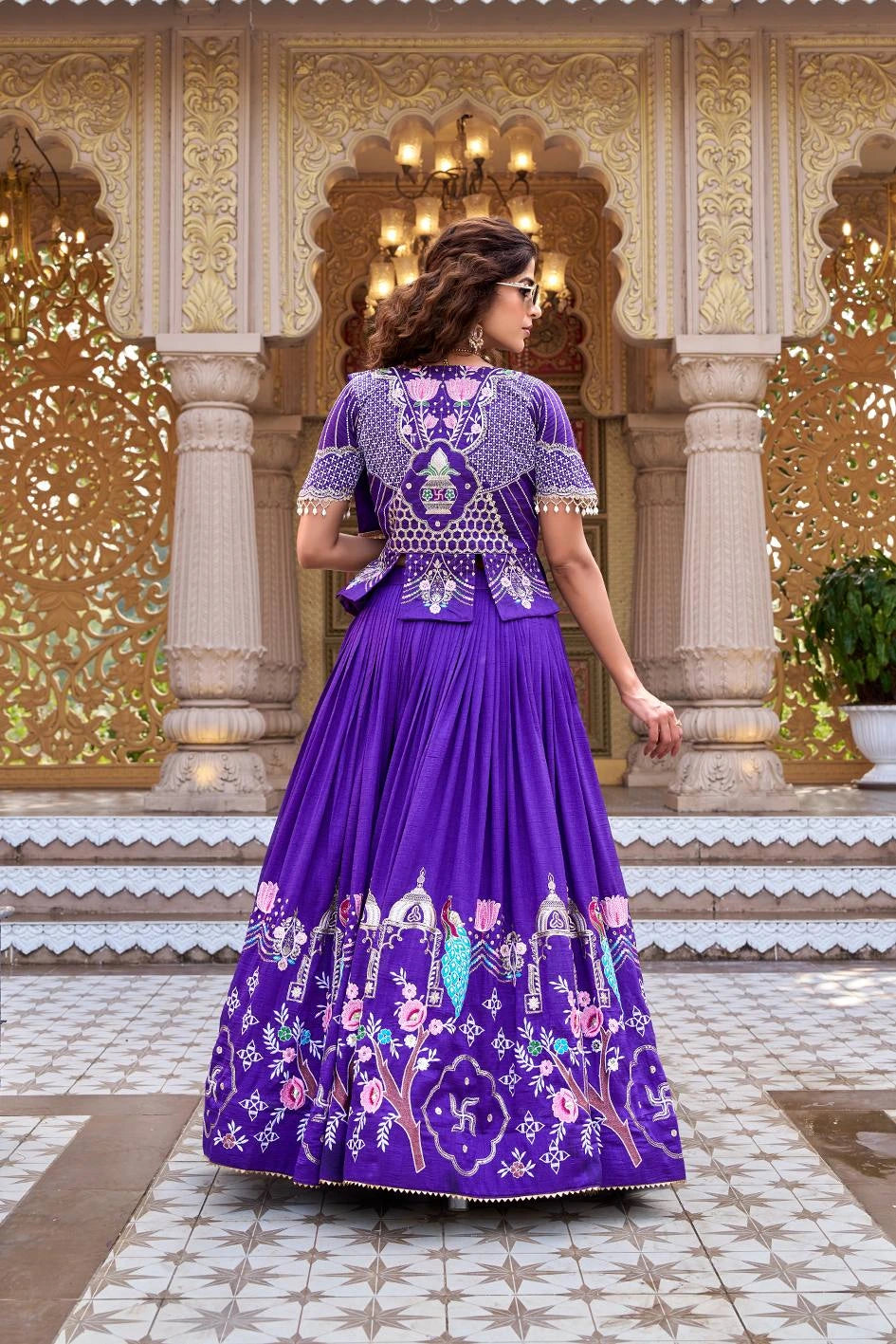 A rear view of the woman in the indigo set, highlighting the heavy embroidery on the back of the short jacket. The design features a central vase motif surrounded by geometric patterns and a line of pearl edging.