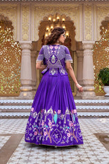 A rear view of the woman in the indigo set, highlighting the heavy embroidery on the back of the short jacket. The design features a central vase motif surrounded by geometric patterns and a line of pearl edging.
