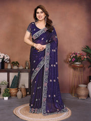 Woman wearing a purple saree with floral patterns in a decorated room.