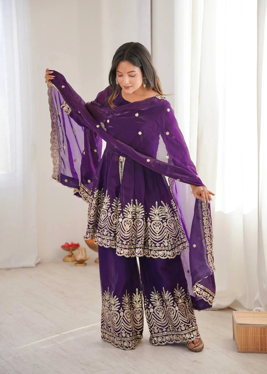 Woman wearing a purple traditional outfit with intricate designs indoors.
