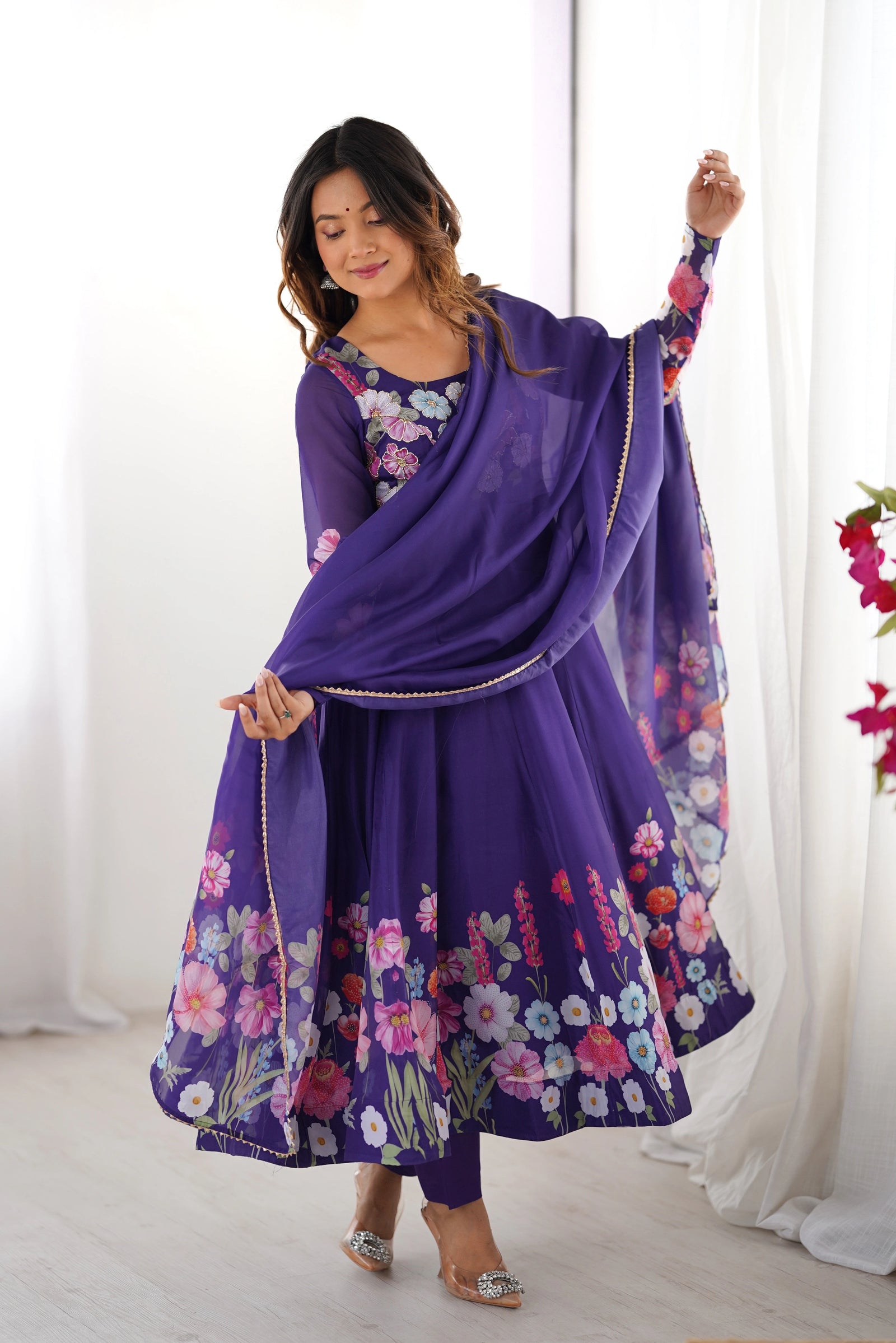 Woman wearing a purple floral outfit with a matching dupatta against a white background