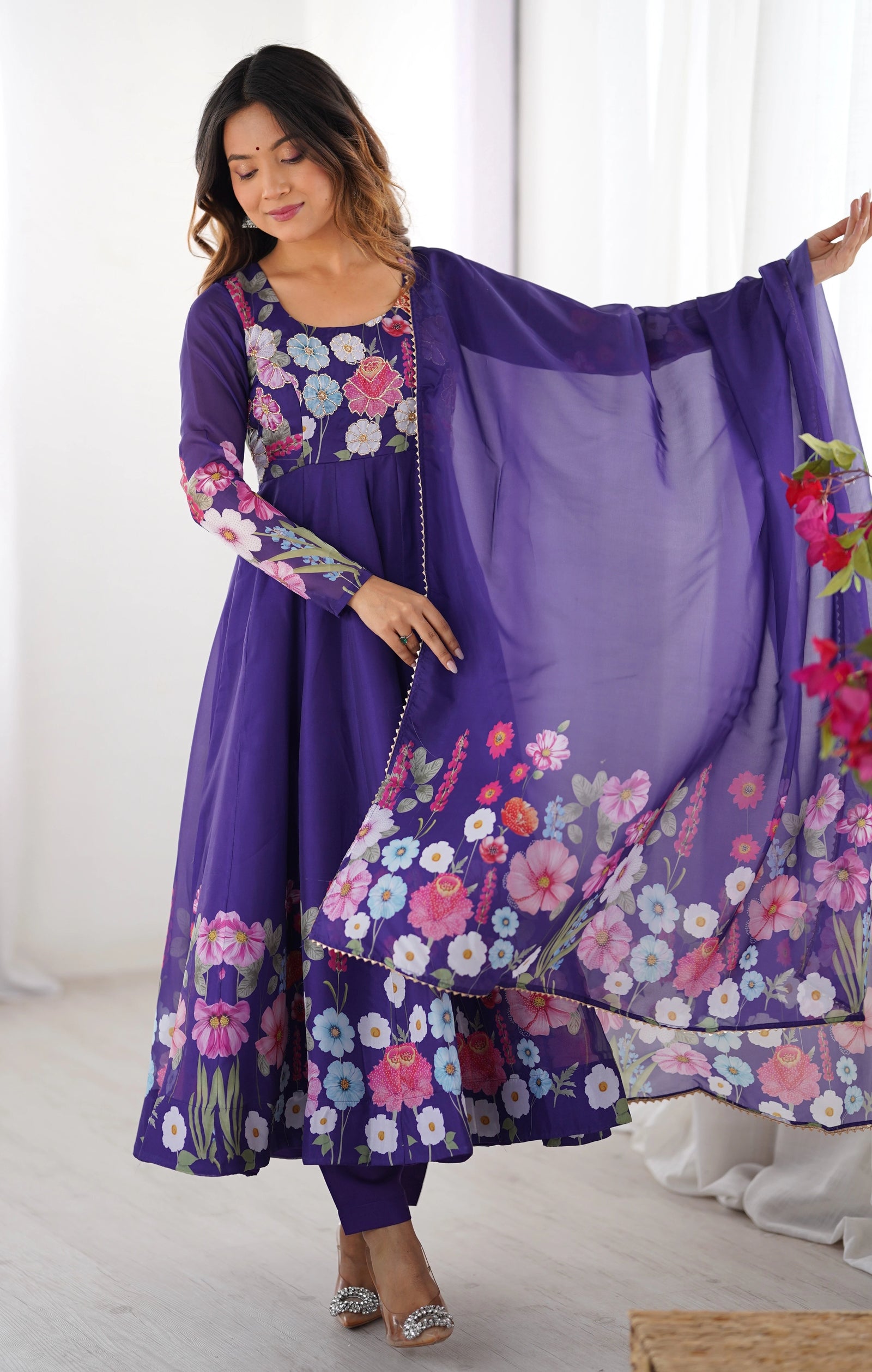 Woman wearing a purple floral dress with a matching dupatta against a white background