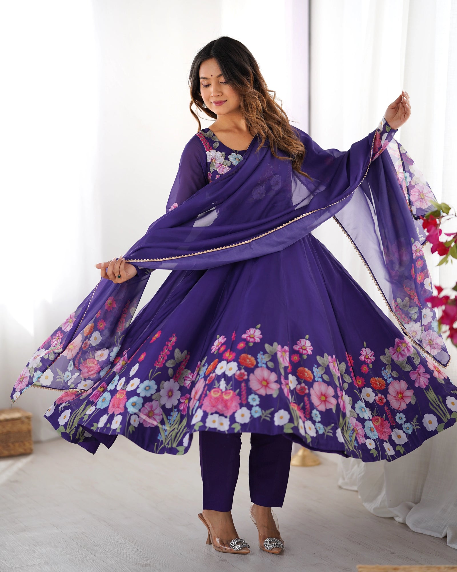Woman in a purple floral outfit with a matching dupatta in a bright room.