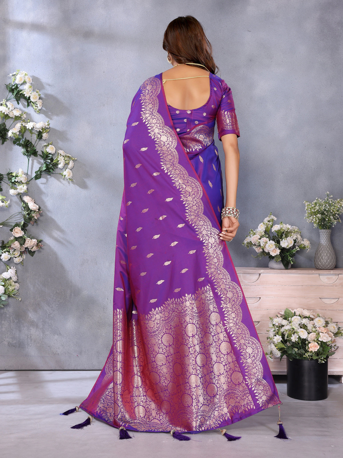 Woman wearing a purple saree with white patterns in a decorated room.