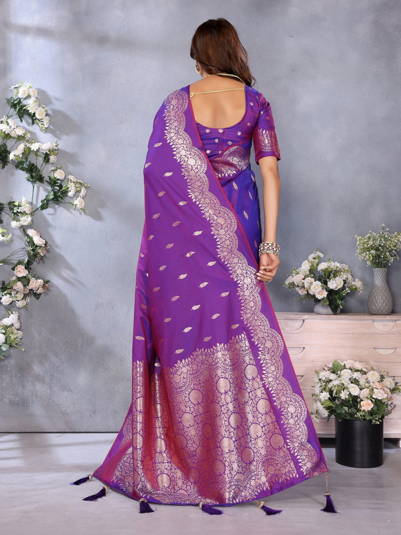 Woman wearing a purple saree with white patterns in a decorated room.