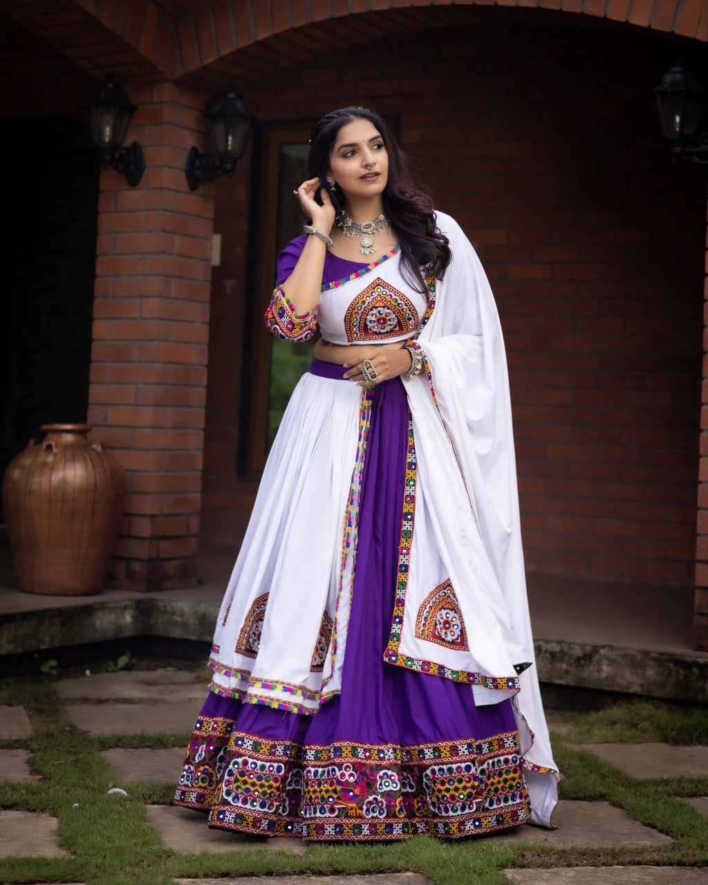 Woman in a traditional outfit with white and purple colors standing outdoors.