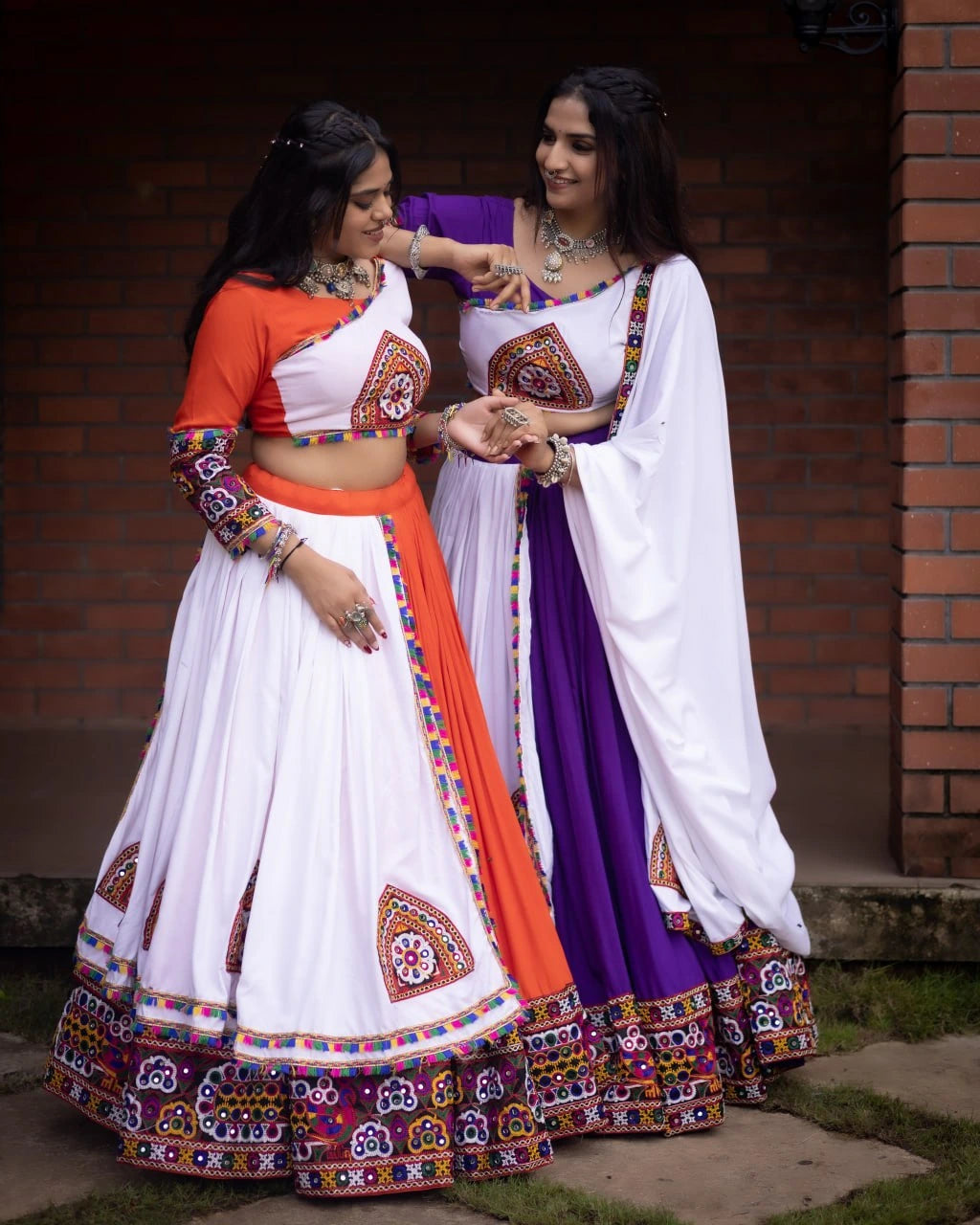Two women in traditional Indian attire standing against a brick wall.