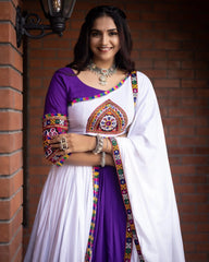 Woman wearing a traditional outfit with a colorful blouse and white saree against a brick wall.