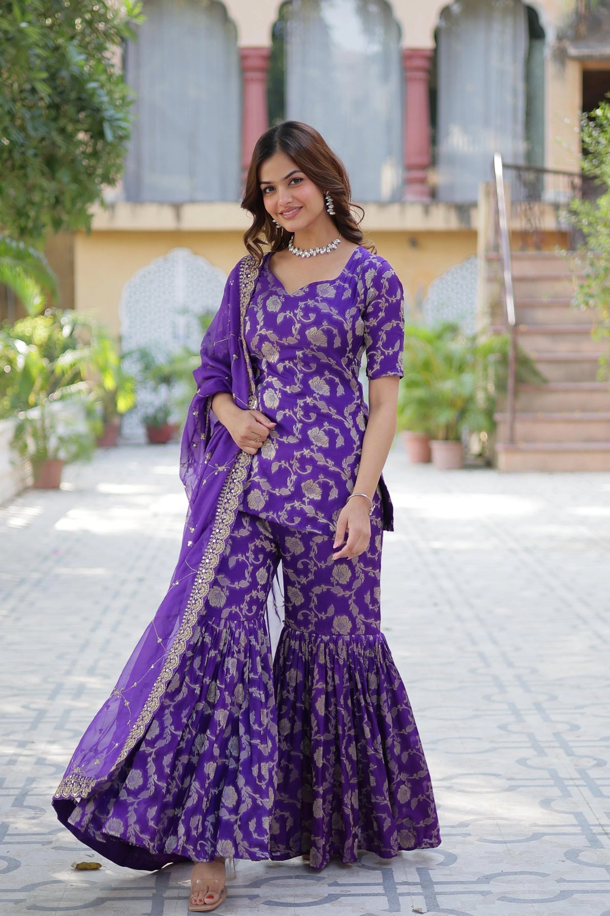 Woman in a purple traditional outfit standing outdoors.