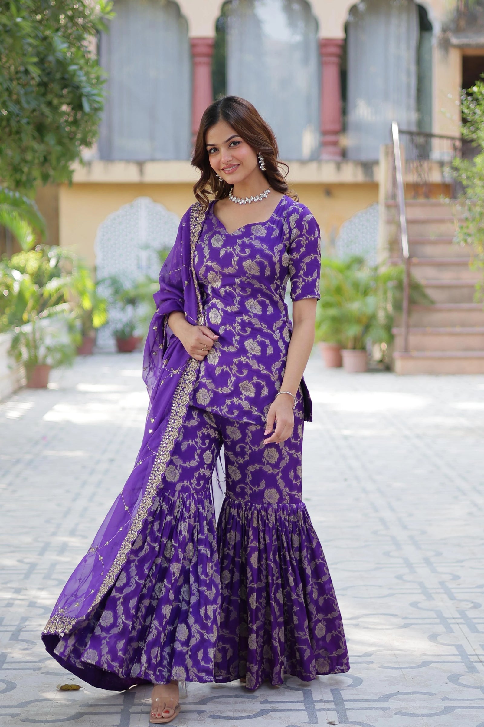 Woman in a purple traditional outfit standing outdoors.