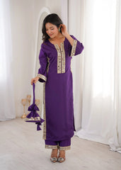 Woman wearing a purple traditional outfit with gold embroidery in a white room.