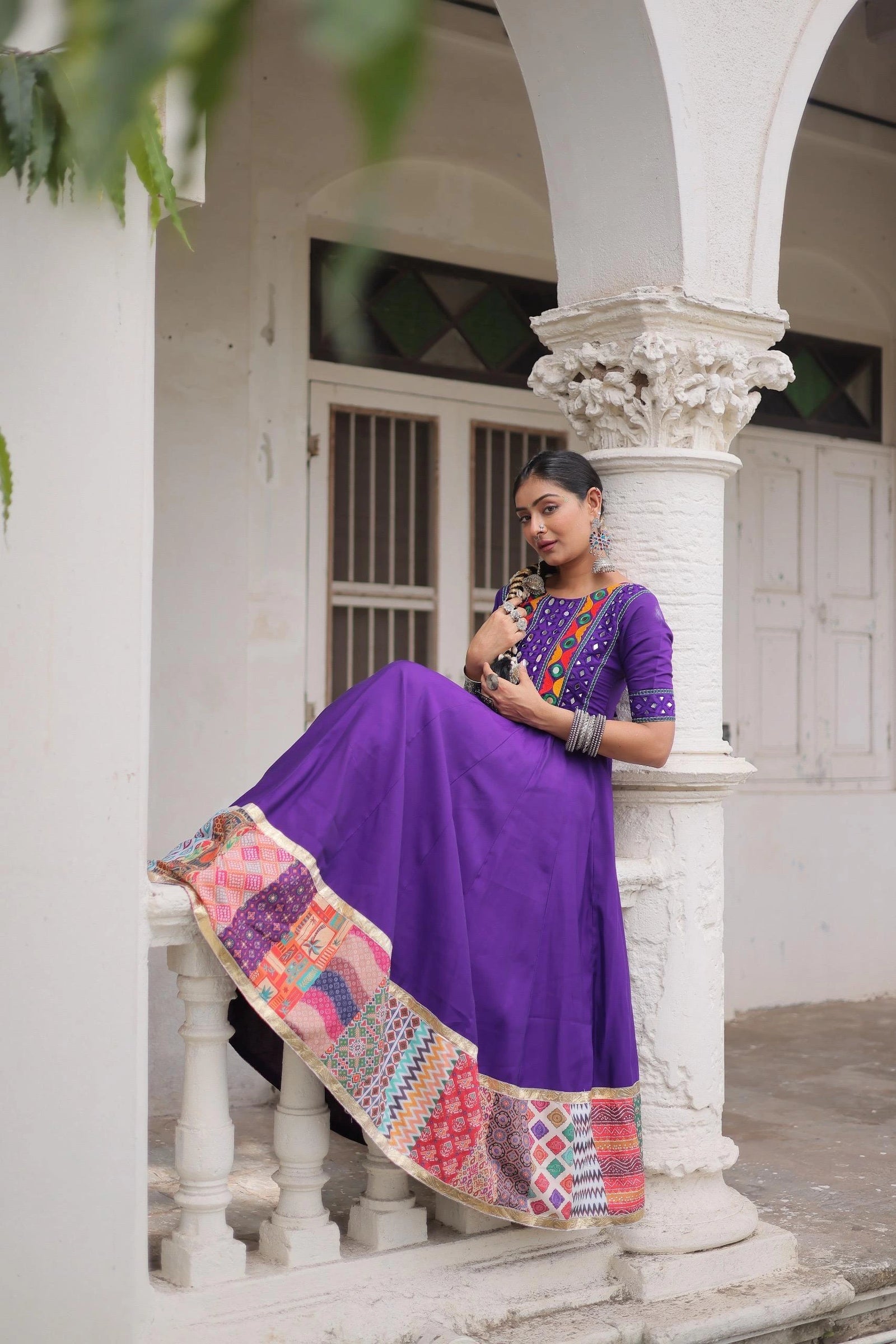 Woman in a purple traditional outfit with a colorful scarf sitting on a white architectural structure.