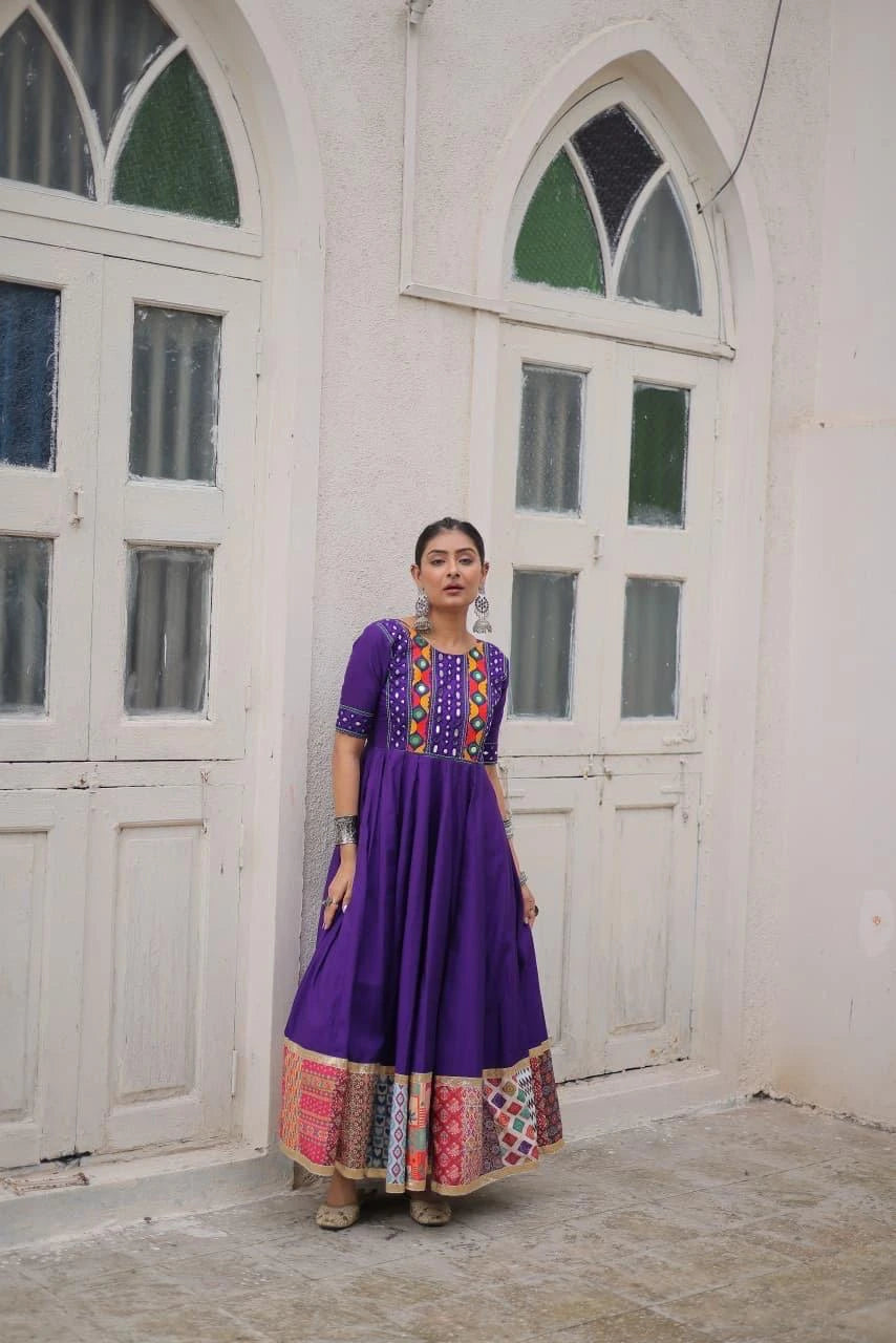 Woman in a colorful dress standing in a room with white walls and large windows.