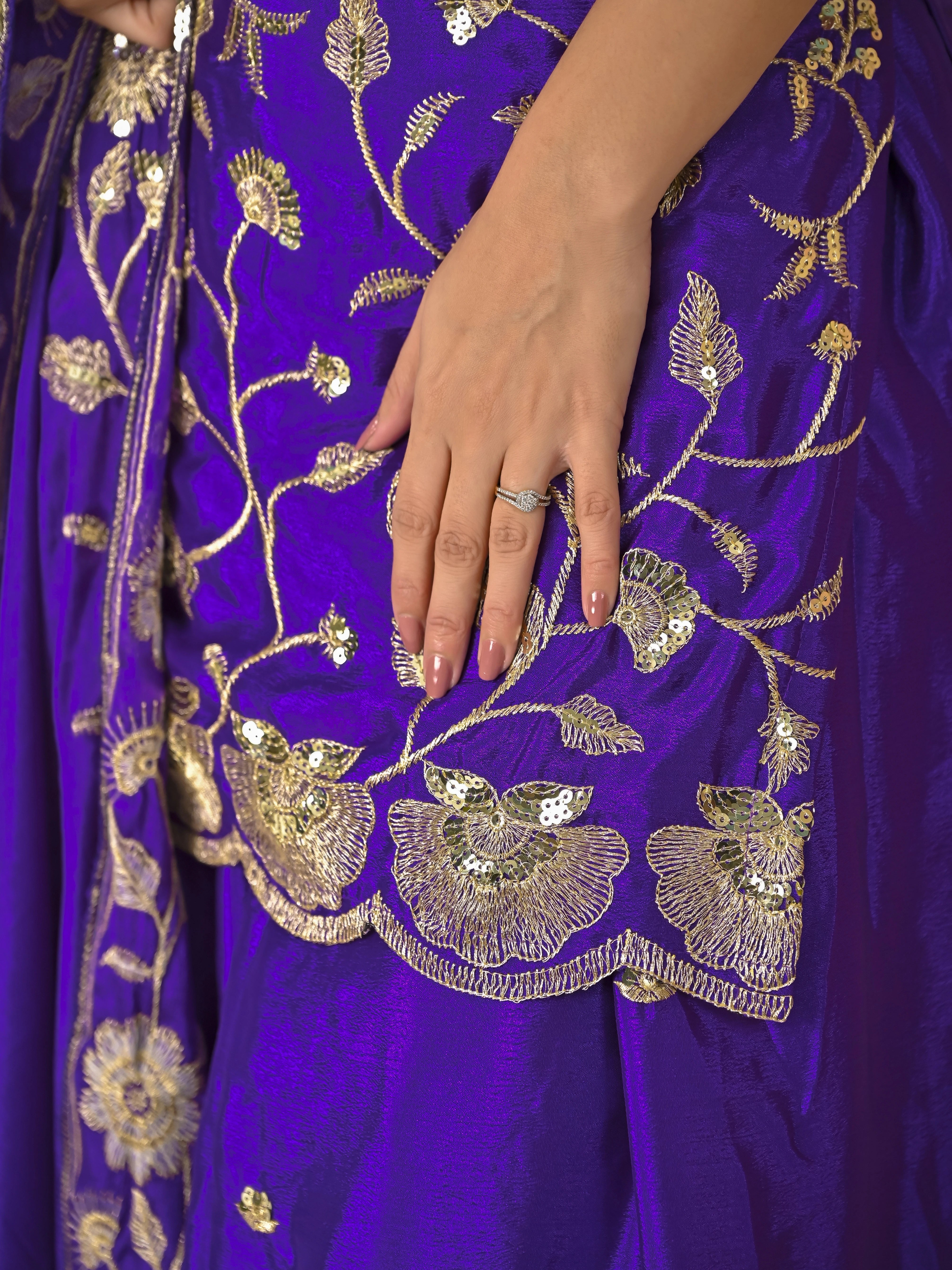 Close-up of a purple fabric with gold embroidery, featuring a hand holding the fabric.