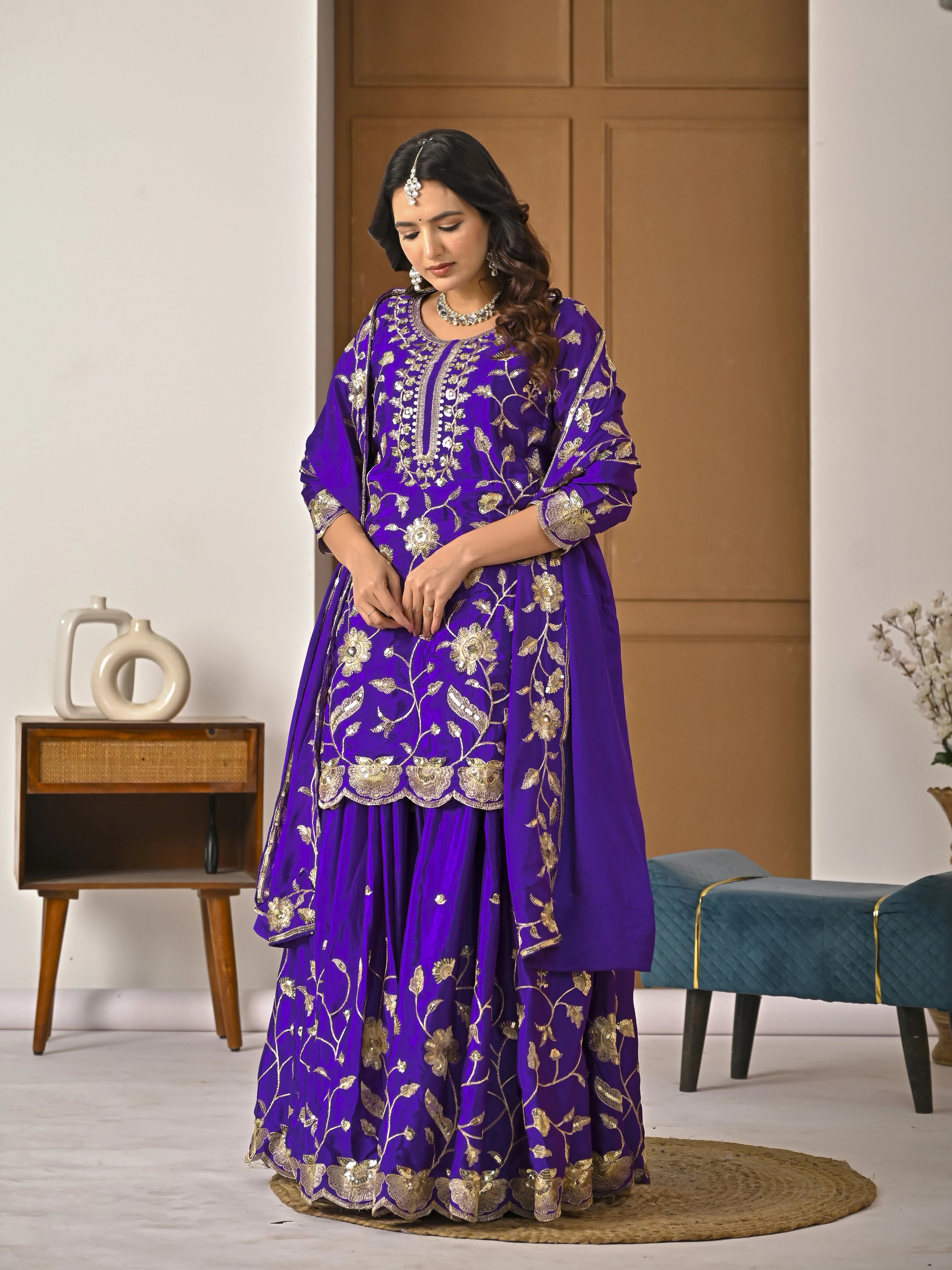 Woman wearing a purple embroidered traditional outfit in a room setting.