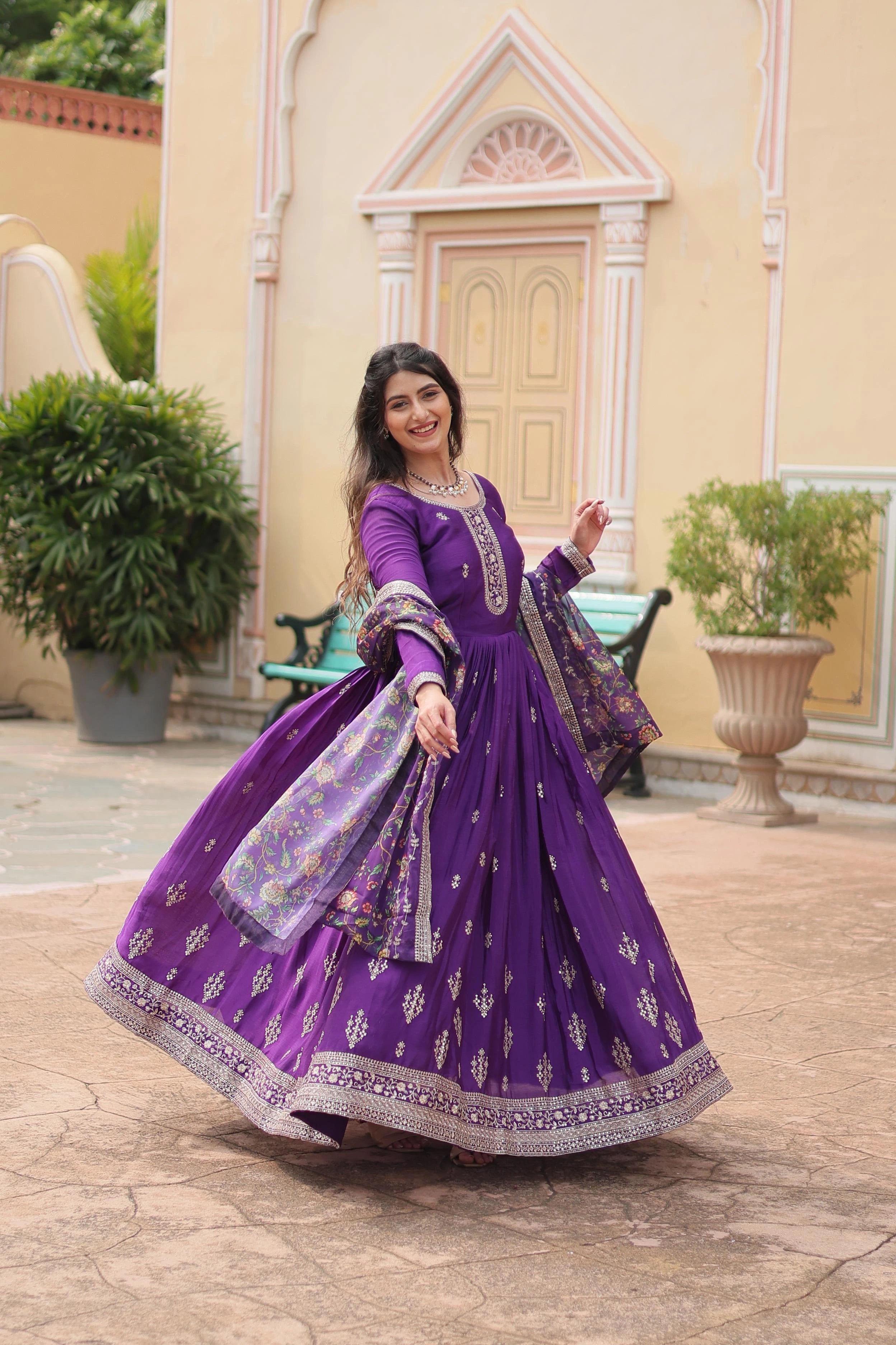 Woman in a purple traditional outfit standing outdoors with decorative elements in the background
