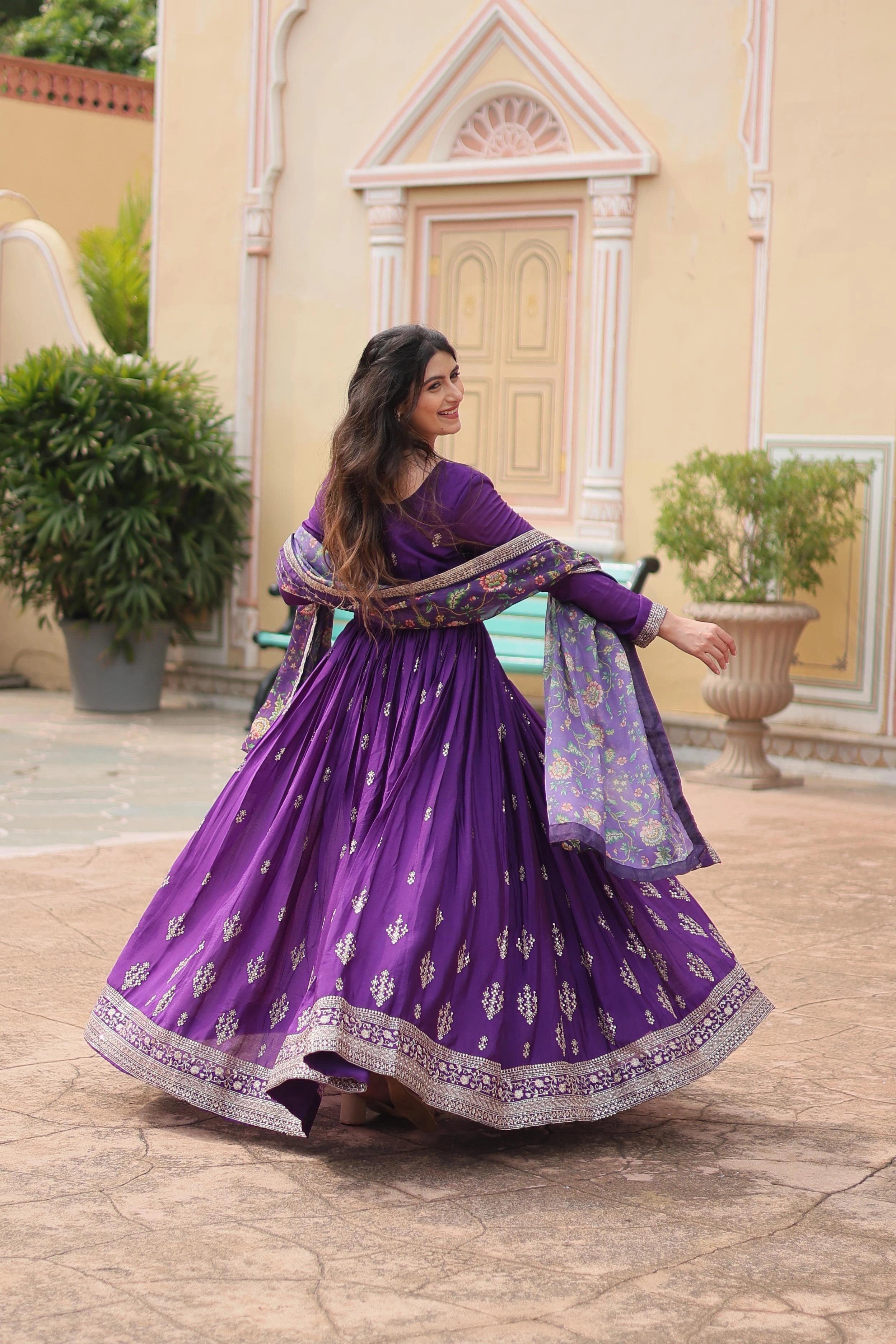 Woman in a purple traditional outfit standing outdoors with decorative elements in the background