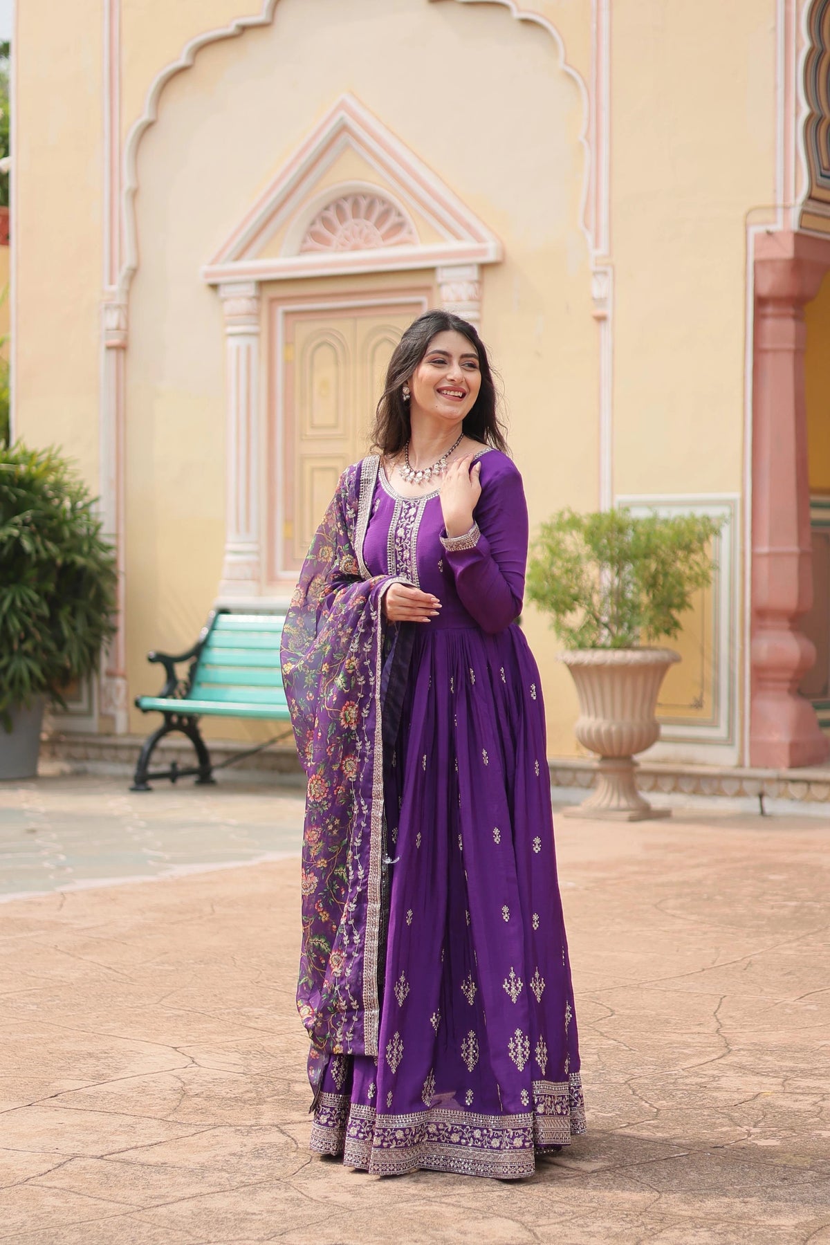 Woman in a purple traditional outfit standing in front of a decorative building entrance.