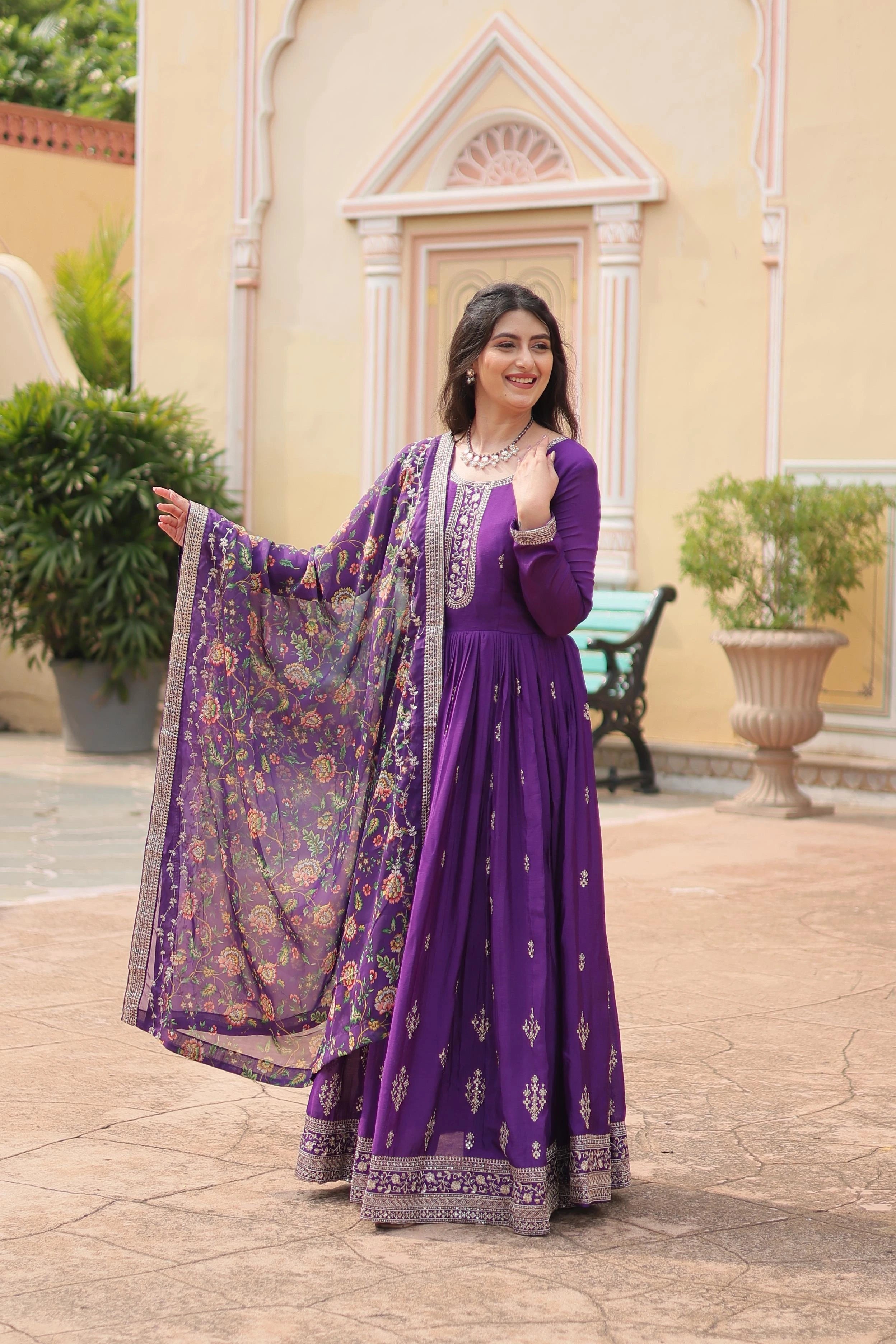 Woman in a purple traditional outfit standing outdoors with decorative elements in the background